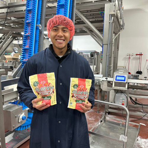A photo of Jacob Gutierrez in the Nestle packaging factory, holding two Outshine products.